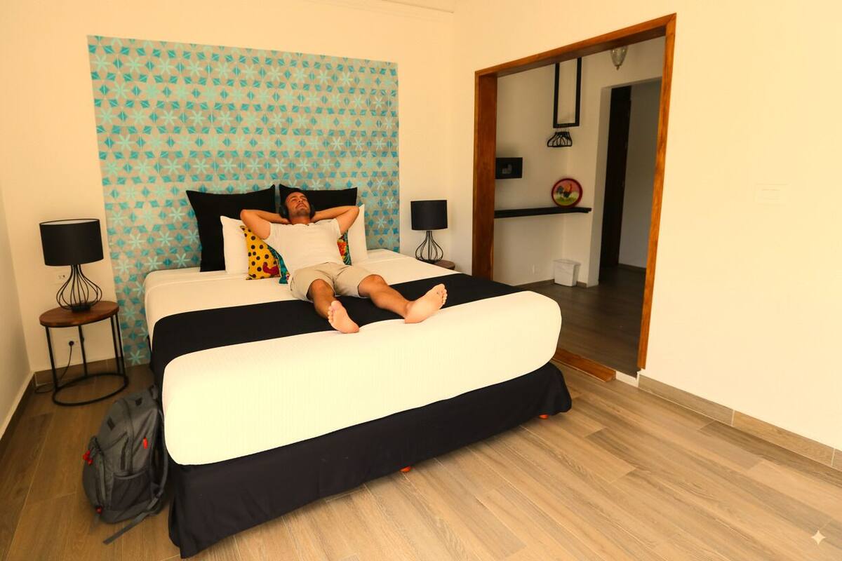 Un lit recouvert d’une couvre-lit noir et blanc, avec une tête de lit bleue à motifs et un plancher en bois.