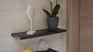 A bathroom with a dark wooden shelf holding a white sculpture, a potted orchid, and two lit candles.