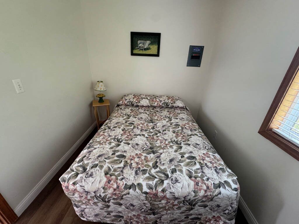 A small, single-bed room with a floral bedspread, a small table with a lamp, and a picture on the wall.
