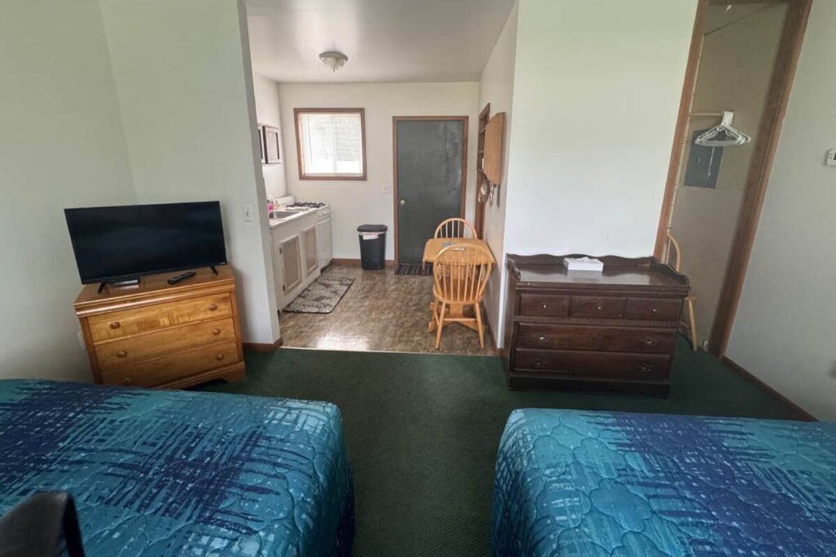A room with two beds, a TV on a dresser, a chair, a desk, and a door.