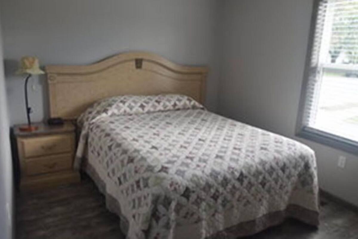 A bedroom with a wooden bed, a nightstand, and a window with blinds.