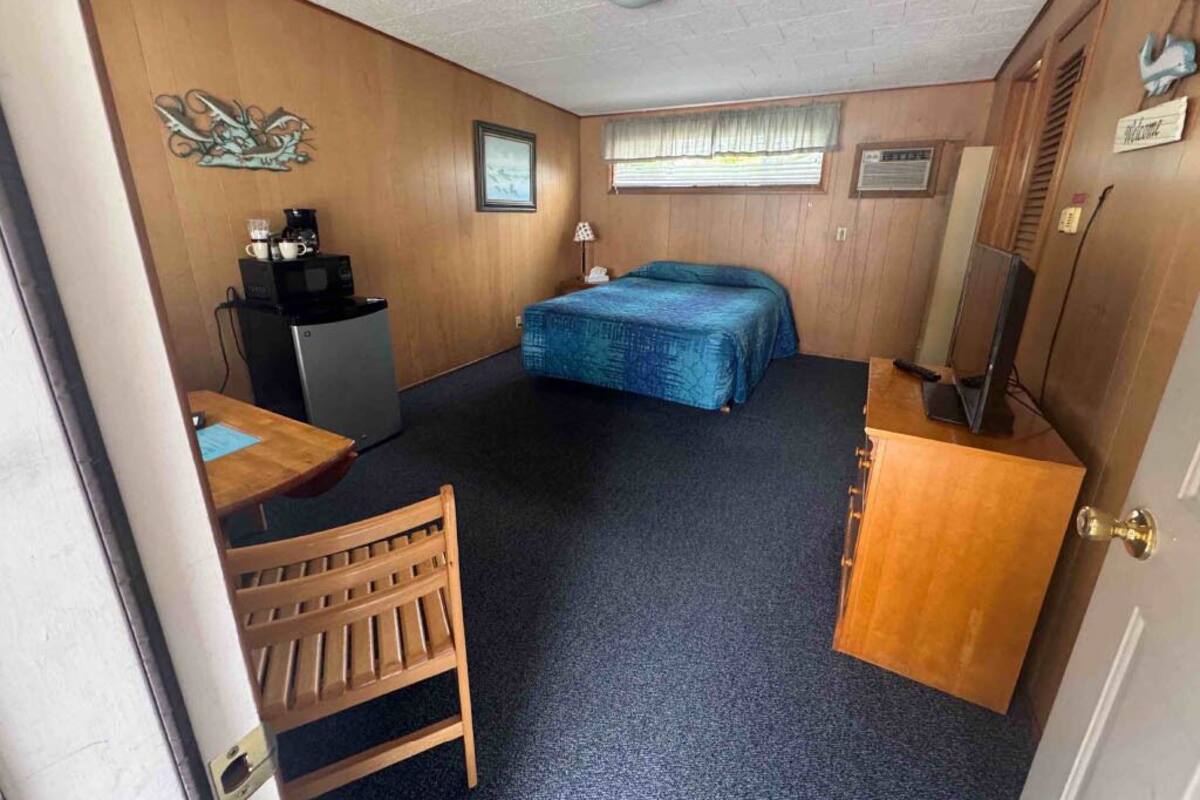 A compact room with a bed, a desk, a chair, a coffee maker, and a television.