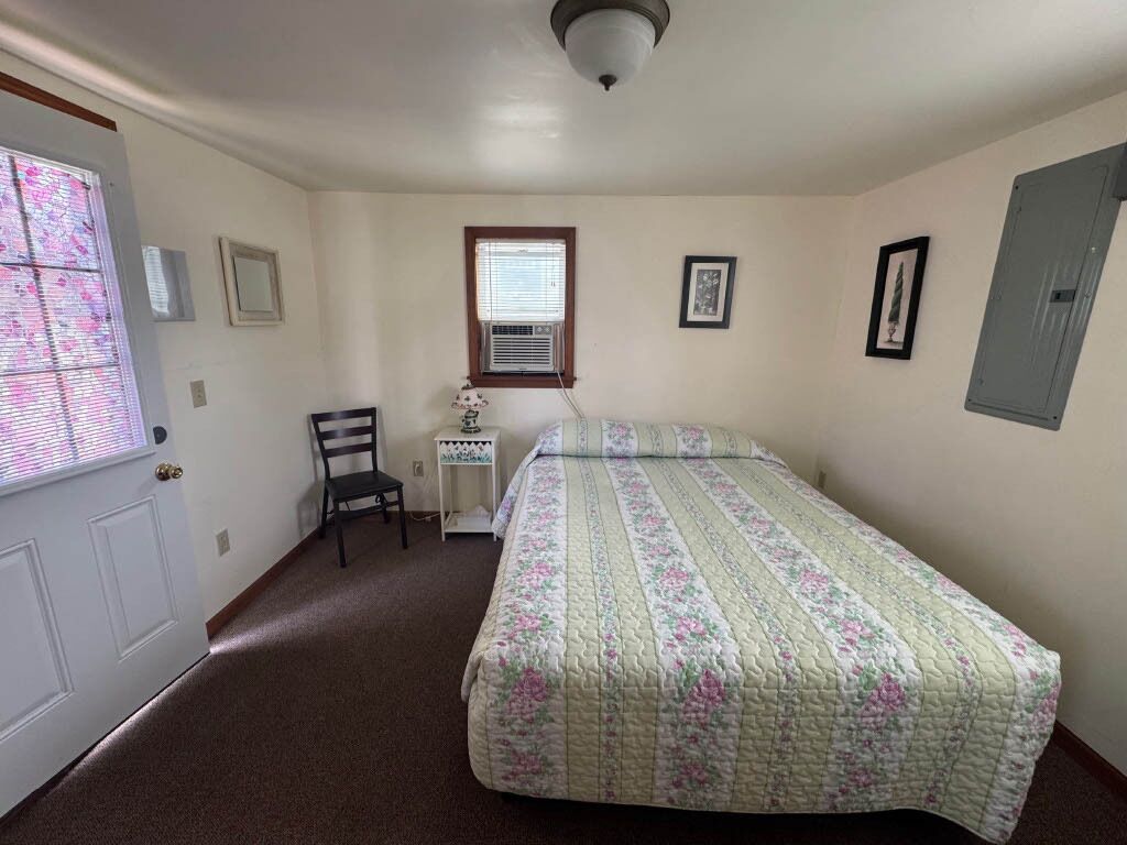 A bedroom with a bed, a chair, a desk, and a window.