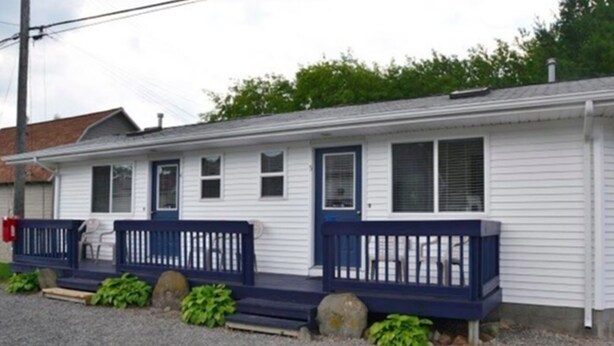 A single-story house with a front porch, a small attached garage, and a gravel driveway.