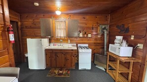 A compact kitchen with wooden walls, a refrigerator, stove, microwave, and a sink.