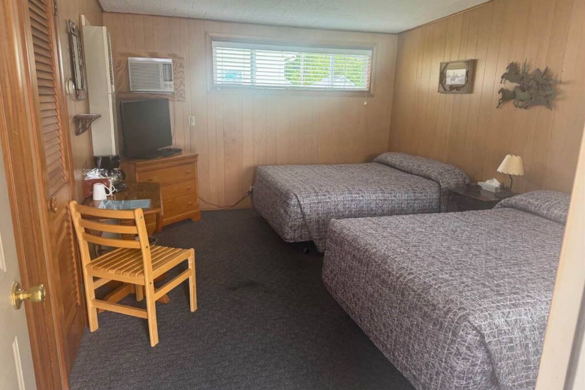 A room with two beds, a desk, a chair, a television, and a window with blinds.