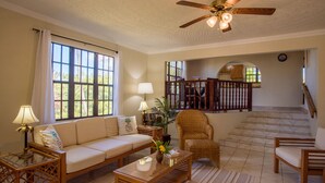 A living room with a sofa, coffee table, and armchairs, a ceiling fan, and a staircase leading to an upper level. - Bayview Vacation Apartments (Virgin Gorda)