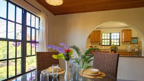 A dining area with a glass table, wicker chairs, and a view of the kitchen through an archway. - Bayview Vacation Apartments (Virgin Gorda)