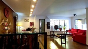 Amplia sala de estar con un sofá rojo, una mesa de centro de vidrio y una mesa de comedor de madera. Una ventana grande ofrece luz natural y vistas al exterior.