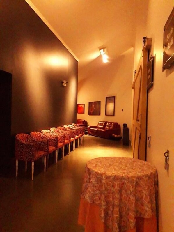 A dimly lit room with a row of red upholstered chairs, a brown leather sofa, and a small table with a patterned tablecloth. - Hotel Aitue (Temuco)