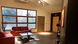 Una sala de estar moderna con un sofá rojo, una mesa de centro y un ventanal con vistas a árboles y un edificio.