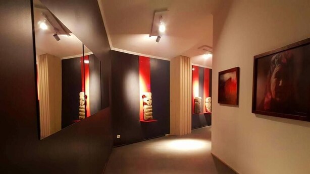 Un pasillo con paredes espejadas, un rincón rojo decorativo y una obra de arte enmarcada a la derecha.