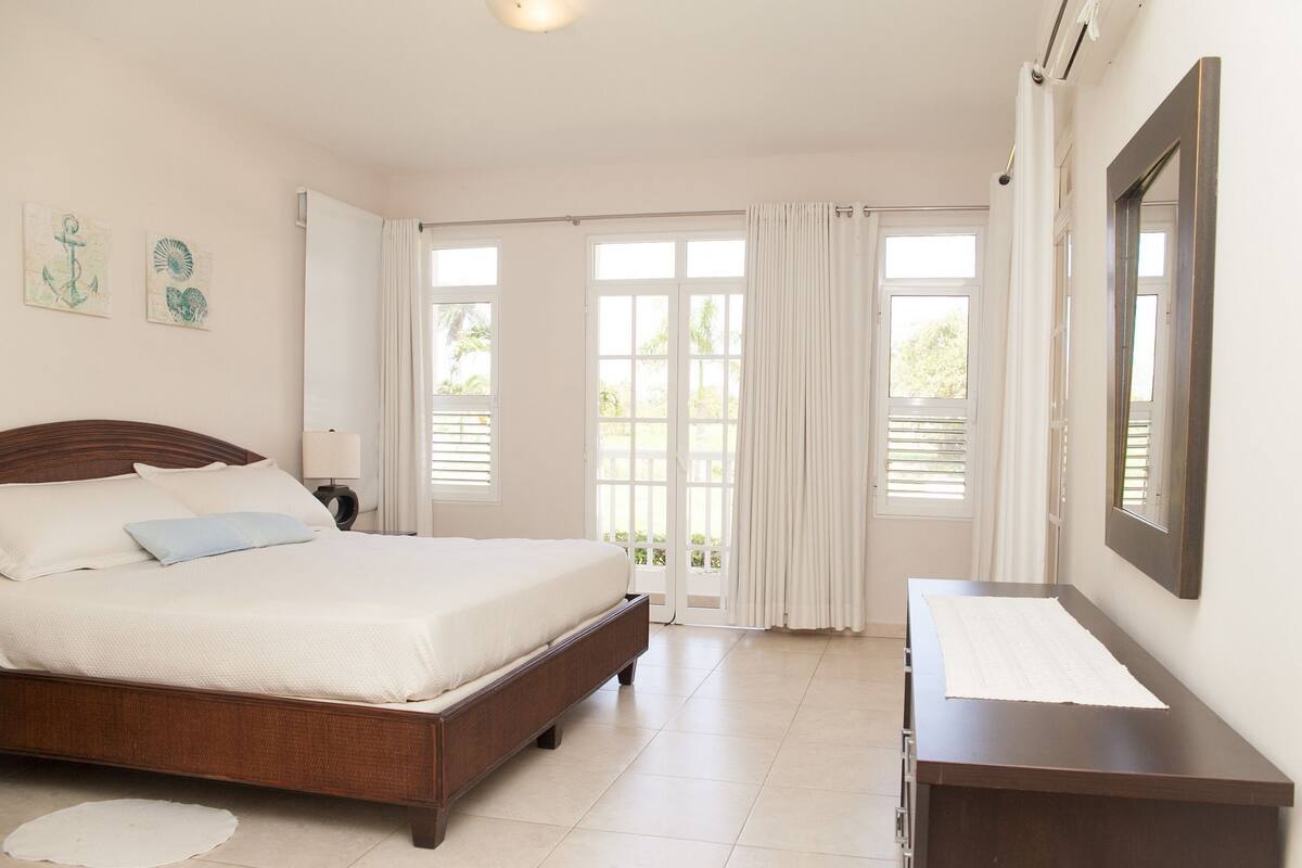 A bedroom with a wooden bed, a bedside table, a mirror, and a view through the glass doors.
