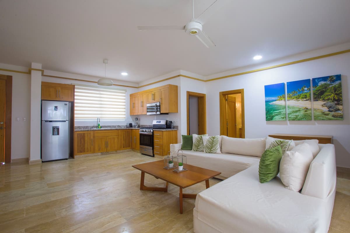 A spacious living area with a sofa, a coffee table, wooden cabinets, a refrigerator, an oven, and a microwave.