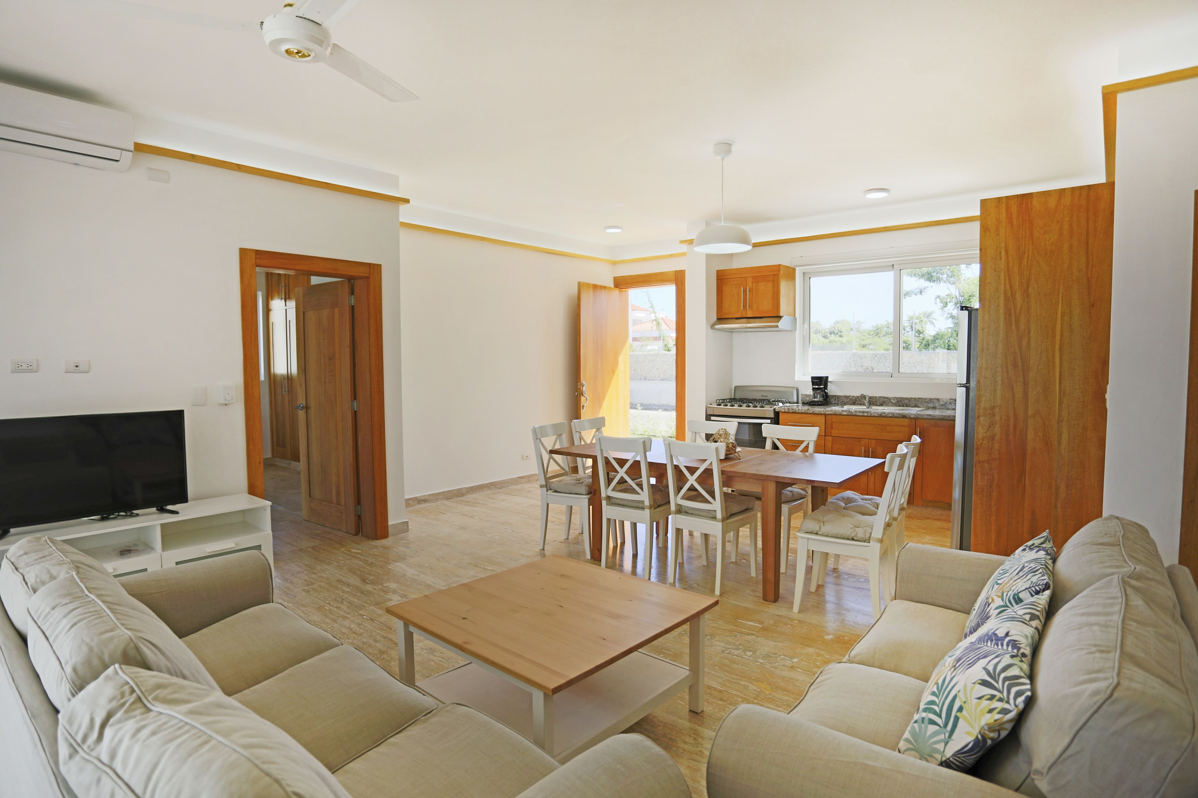 Una sala de estar moderna con un sofá, un televisor, una mesa de madera y un comedor con sillas.