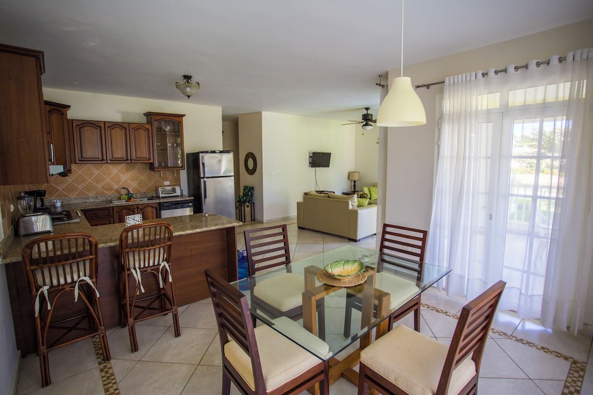 A modern kitchen with wooden cabinets, a glass dining table, and a seating area with chairs.