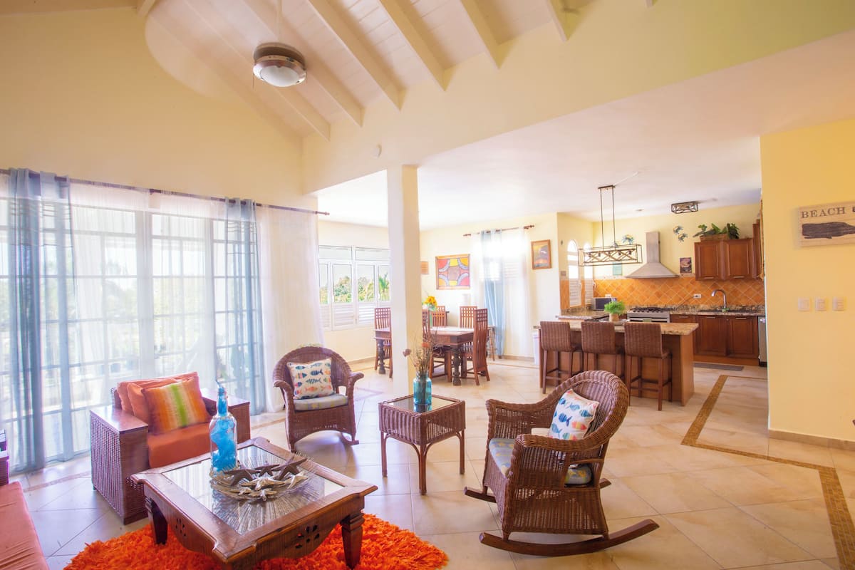 A spacious living area with a dining table, wicker furniture, and a kitchen in the background.