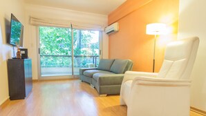 Een moderne woonkamer met een bank, een witte fauteuil, een televisie en een lamp.