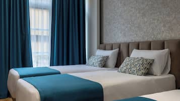 A hotel room with two beds, a large window with curtains, a textured wall, and a view of buildings.