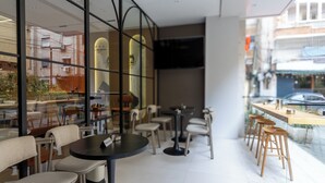 Um café moderno com mesas redondas e banquetas, janelas amplas com reflexos e vista para a rua.