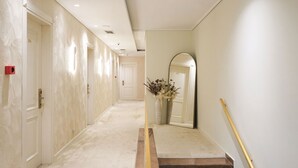 Corredor de hotel com piso de mármore, portas brancas e um espelho na parede.
