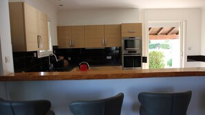 Eine moderne Küche mit Holzschränken, einem eingebauten Backofen und einer Bar mit drei schwarzen Barhocker.