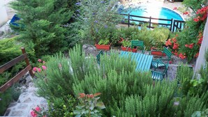 Un patio trasero con piscina, una terraza de madera y diversas plantas.