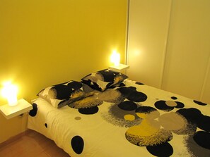 Ein Bett mit schwarz-weiß gemustertem Überwurf, zwei Nachttischlampen und ein weißer Nachttisch.