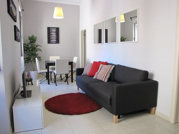 Ein modernes Wohnzimmer mit einem dunkelgrauen Sofa, einem roten Teppich und einem Essbereich mit weißen Stühlen und einem Tisch.
