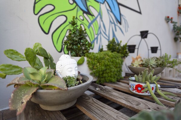 A variety of potted plants on a wooden table, with a Buddha statue in one pot and a colorful flower pot in another.