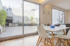 A modern kitchen with a large window, a dining area with white chairs and a table, and a view of the backyard. - Ravignani by Be Local Argentina (Buenos Aires)