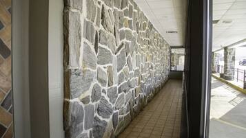A corridor with a stone wall and tiled floor, leading to a glass door.