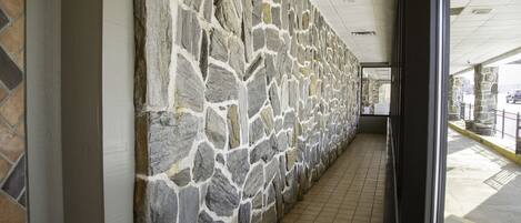 A corridor with a stone wall and tiled floor, leading to a glass door.