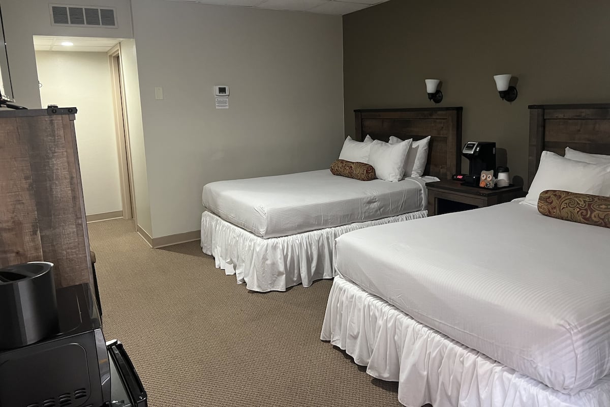 A hotel room with two beds, a desk, a coffee maker, and a TV.