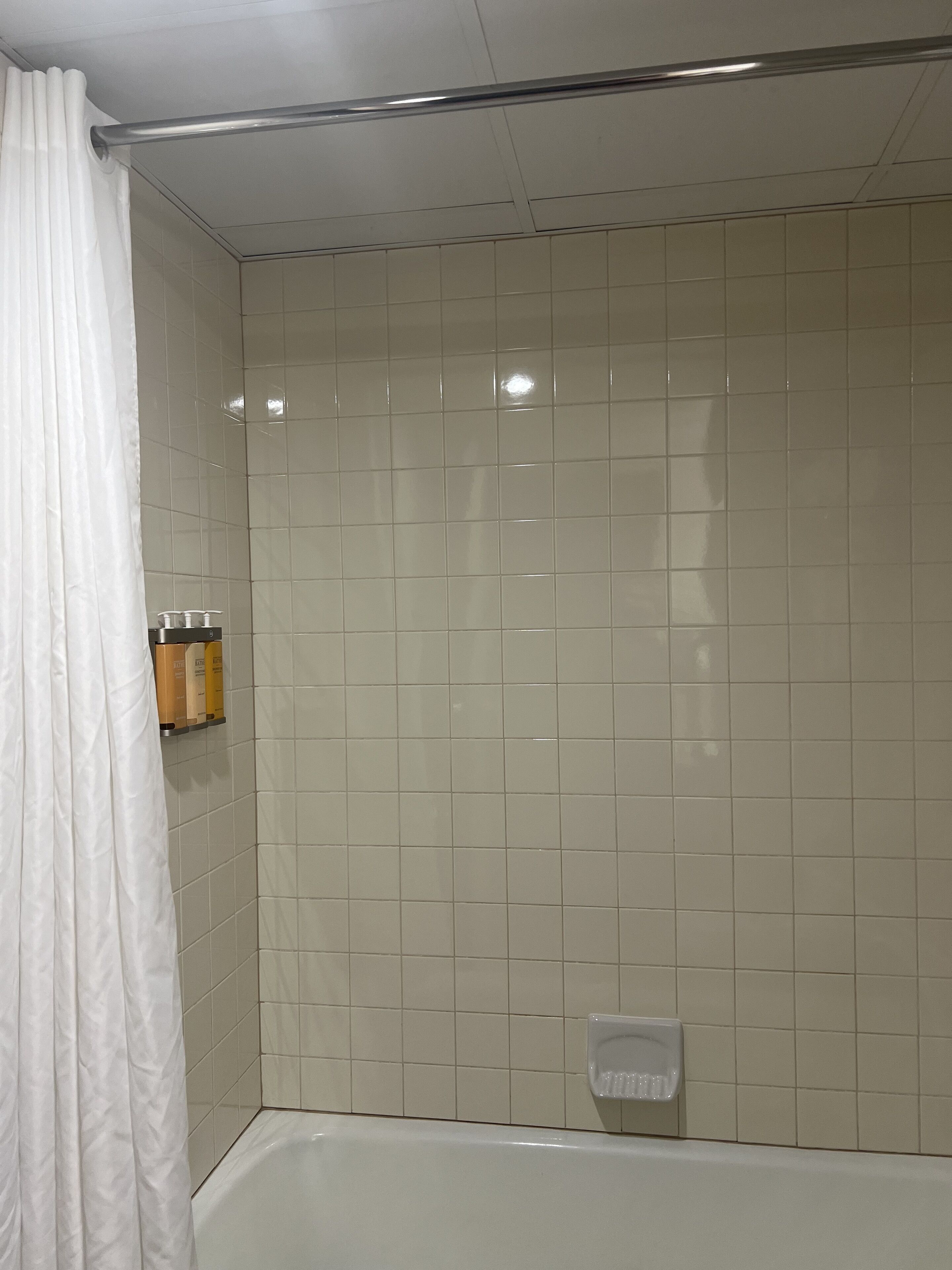 Un baño con bañera, paredes de azulejos blancos, una cortina de ducha y un dispensador de jabón en la pared.