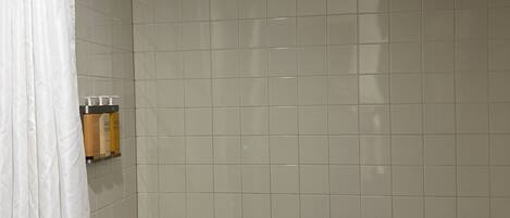 Un baño con bañera, paredes de azulejos blancos, una cortina de ducha y un dispensador de jabón en la pared.
