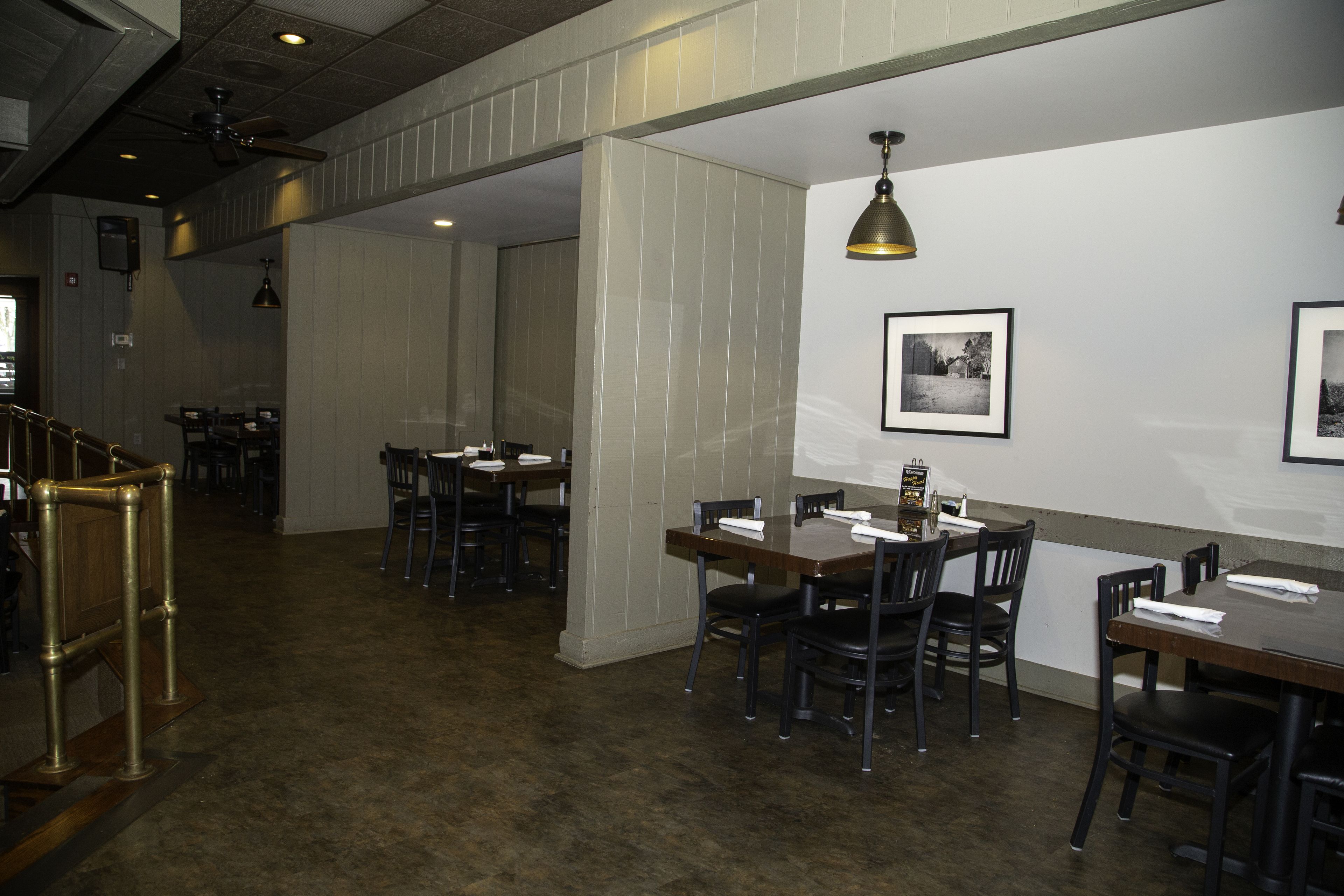 A restaurant interior with wooden tables and chairs, a ceiling fan, and framed pictures on the walls.