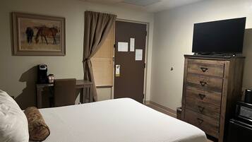 Quarto de hotel com cama, escrivaninha com cafeteira, televisão em uma cômoda e um quadro na parede.