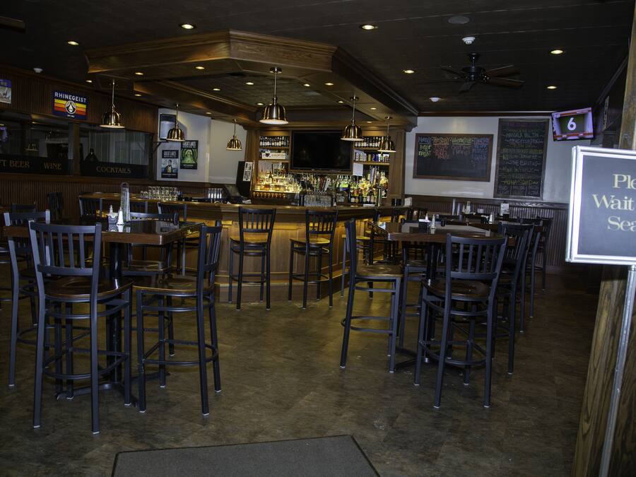 A bar area with wooden furniture, a counter with bottles, and a sign indicating seating availability.