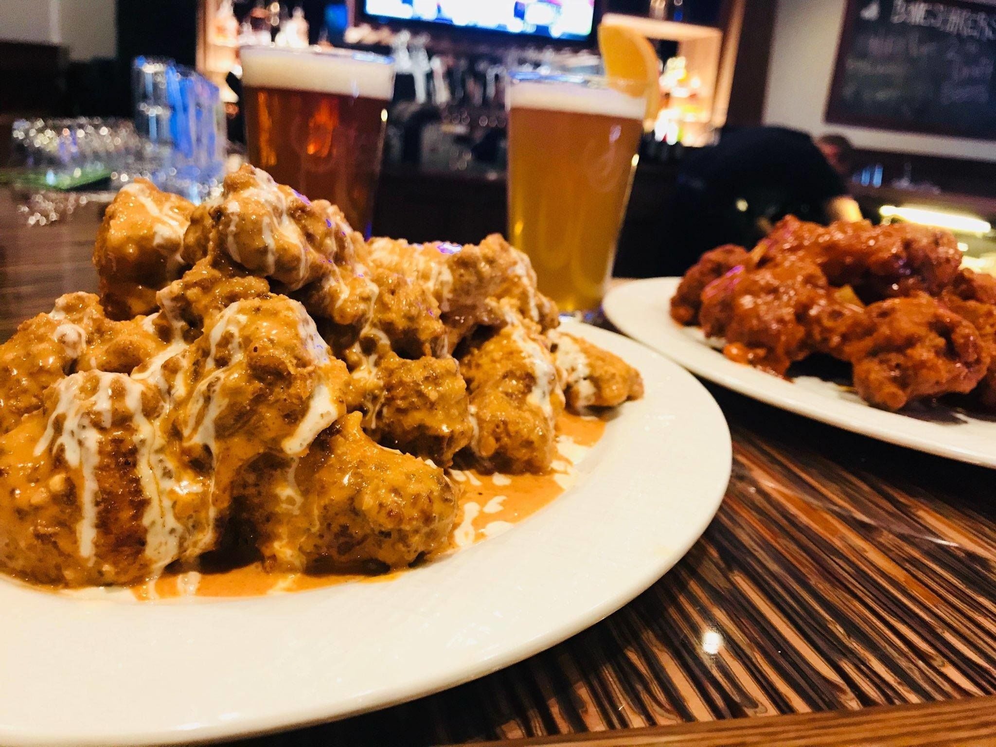 Un plato de pollo frito con salsa cremosa y una cerveza sobre una mesa de madera.