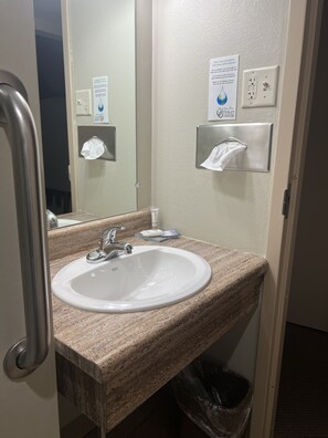 Une salle de bain équipée d’un lavabo, d’un miroir, d’un distributeur de serviettes et d’une poubelle.