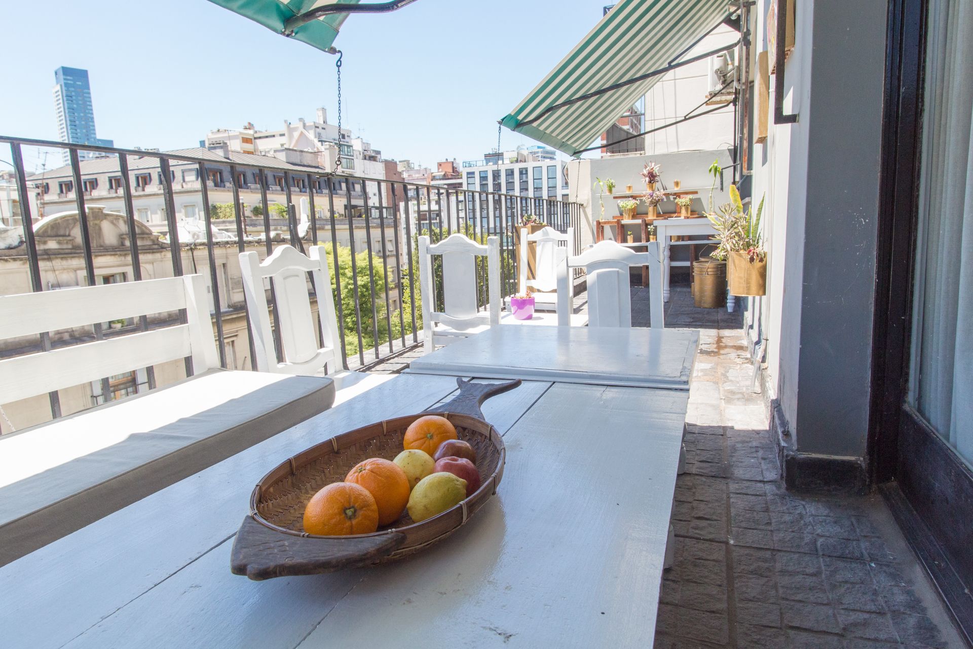 A balcony with a wooden boat filled with fruits, white chairs, and a table with potted plants.