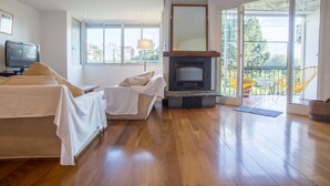 Een ruime woonkamer met een open haard, houten vloeren, een bank en een televisie.