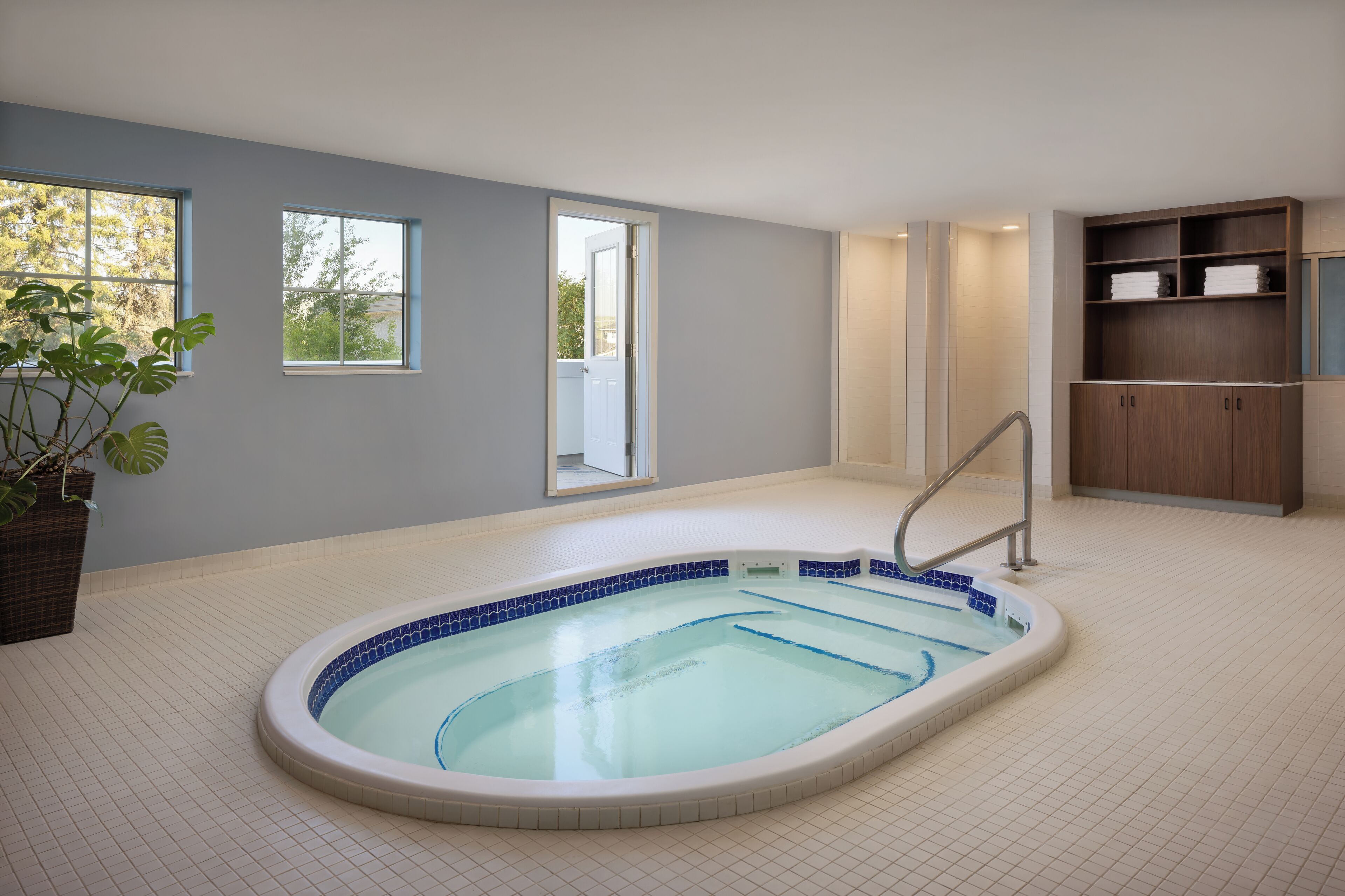 A modern indoor swimming pool with a tiled floor, a wooden cabinet, and a potted plant.