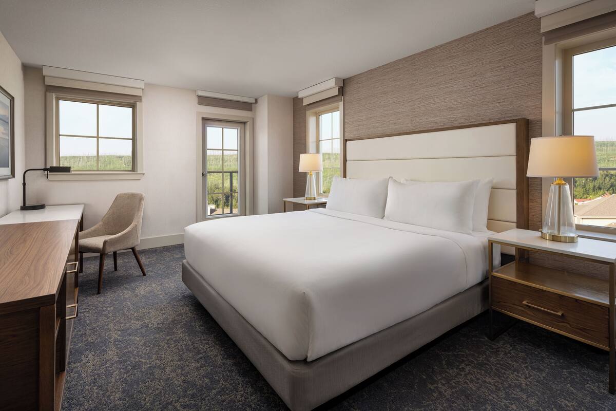A hotel room with a large bed, a desk, a chair, and two bedside lamps.