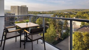 A balcony with a table and chairs, overlooking a cityscape with buildings and trees. - Pomeroy Hotel Fort McMurray (Fort McMurray)