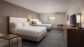 A hotel room with two beds, a desk, a chair, a TV, and a window with a view.