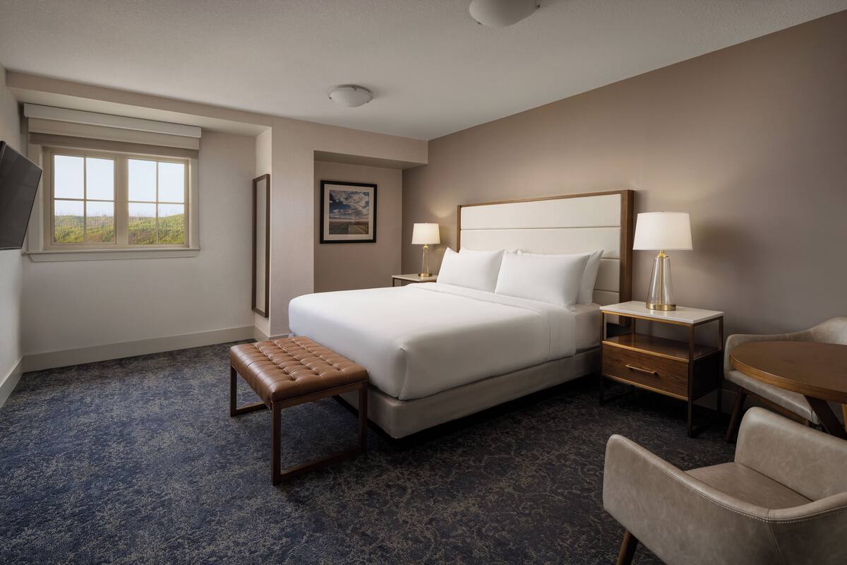 A hotel room with a large bed, a bench, a desk, and a chair.