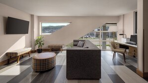 A modern living room with a sofa, a bench, a coffee table, and a desk with a computer. - Pomeroy Hotel Fort McMurray (Fort McMurray)