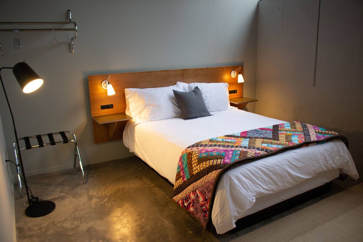 A neatly made bed with a colorful quilt, two bedside lamps, and a small bedside table.